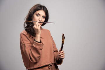 Young woman holding paint brushes and looking at camera