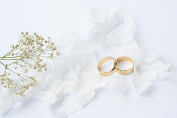 two gold wedding rings on a white background and a flower on the left