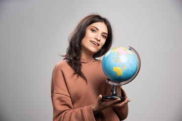 Brunette woman holding globe on gray background