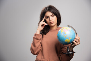 Brunette woman looking at globe on gray background