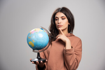 Brunette woman looking at globe on gray background