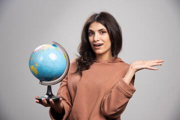Brunette woman holding globe on gray background