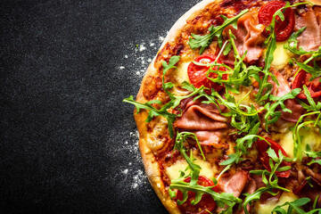 Pizza on black background. Traditional italian pizza with ham, cheese, tomatoes and arugula. Flat...