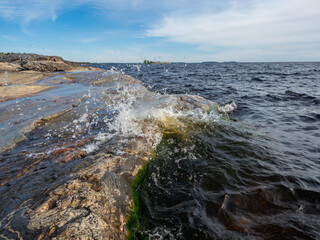 Small waves crashing on the rocky shore on the Ladoga Lake in Karelia, northwest Russia in summer. Nice, hot, sunny weather in July. Clouds on the sky