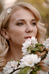 Obraz na płótnie Canvas Adult blonde woman portrait enjoying flowering tree in spring garden