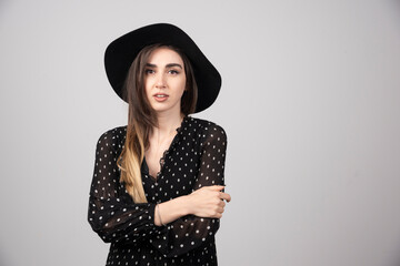 Beautiful young woman in black hat standing arms crossed