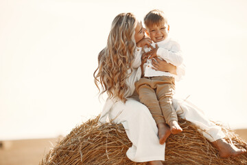 Mom and son are sitting on a haystack in the field at sunset - Powered by Adobe