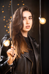 Portrait of a beautiful young model in black leather jacket posing near lamps