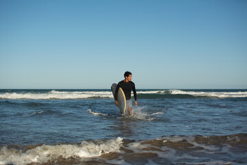 Fototapeta na wymiar Man coming out of the ocean with surfboard facing sideways