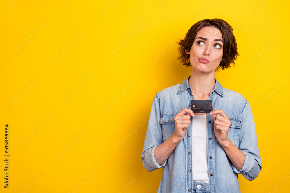 Poster Photo of young lovely woman minded look empty space unsure hold bank card isolated over yellow color background