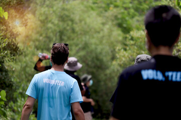 Naklejka premium Back of volunteer man in blue t-shirt doing charity work together with team in the forest, ecology people cleaning and picking up trash to reduce land pollution environmental problem.