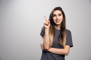 Young woman standing and pointing up over a gray background