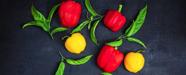 Top view of fresh red bell peppers and yellow bell peppers on a black wooden background.