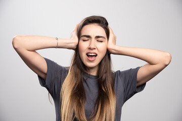 Young woman covering her ears with hands over a gray background