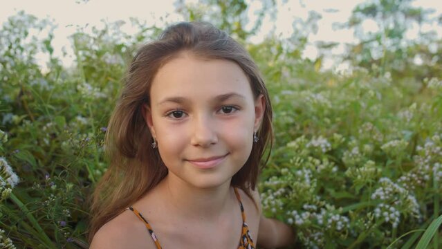 Close-up of happy attractive girl at the flower meadow. The child face smiles and looking at the camera. 4K