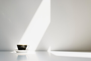 A black porcelain coffe cup on a white table with strong sunlight hitting the wall behind it. Nr.5