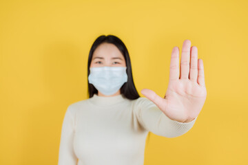 Asian woman in medical face mask to protect Covid-19 show stop hands gesture for stop corona virus outbreak on yellow background