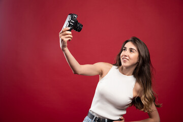 Pretty woman taking selfie with a camera on a red background