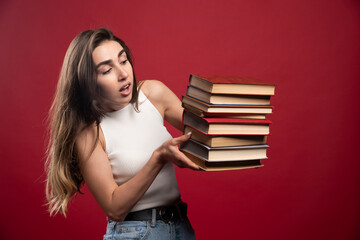 Young pretty woman model carrying a lot of books on a red background