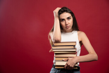 Young girl student holds a stack of books on a red background