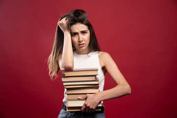 Portrait of a young brunette woman holding lots of books on a red background