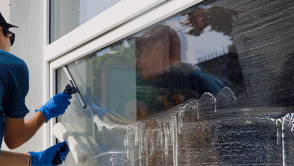 An employee of a professional cleaning service in overalls washes the glass of the windows of the...