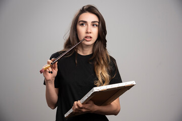 Female artist in black shirt touching her mouth with brush