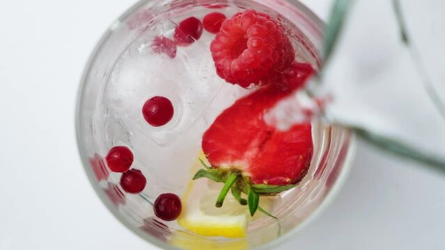 The process of pouring water into a summer cocktail with strawberries, berries, lemon and ice