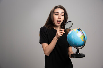 Surprised brunette woman looking at globe with magnifying glass