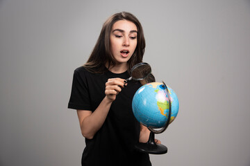 Surprised woman looking at globe with magnifying glass