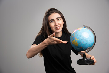 Fototapeta premium Young woman showing globe on gray background