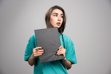 Female doctor posing with clipboard on gray background