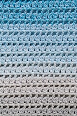 Striped and geometric pattern. Crochet product from multicolored threads. Handmade backdrop. Flat lay. Fragment of a baktus of blue and grey tone. Vertical image