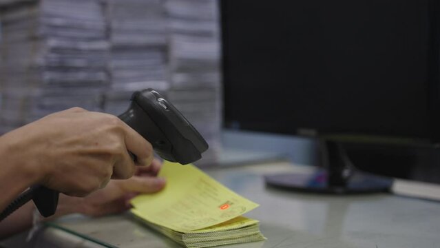 Hand of woman hold bar code reader and scan to reading QR code on stack of yellow documents for transfer data to computer.