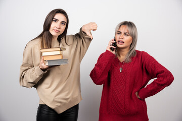 One of girls holding books another girl speaking on phone