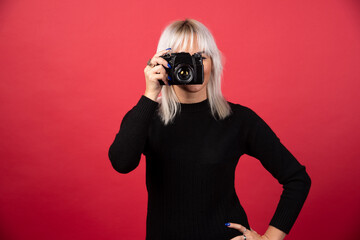 Young woman taking pictures witha camera on a red background