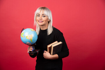Young woman model posing with a books and a Earth globe on a red background