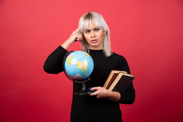 Young woman model posing with a books and a Earth globe on a red background
