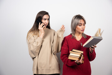 Girl in red sweater reading a book while another girl speaking on phone