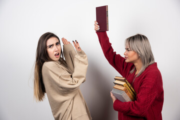 Girl in red sweater hitting another girl with book