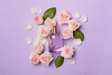 Bottle of perfume with rose flowers on color background, top view