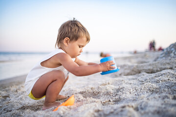 Boy playing with toys on the beach building beads and turrets smiling at someone behind the scenes on summer vacation