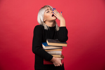 Young woman model holding a lot of books on a red background
