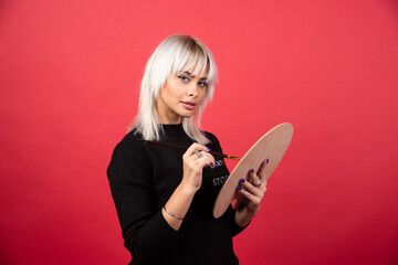 Young artist woman holding art supplies on a red background