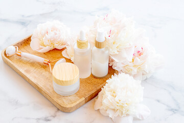 Obraz na płótnie Canvas White cosmetic bottle containers with peony flowers on wooden tray. Cosmetics SPA branding mock-up Natural organic beauty product