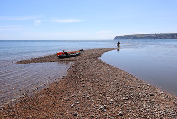 Three canoes rest on the edge of the shingle beach at the mouth of the river Axe in Axmouth. In the...