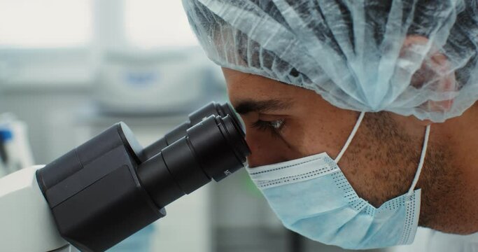 A scientist in sterile clothing looks through a microscope