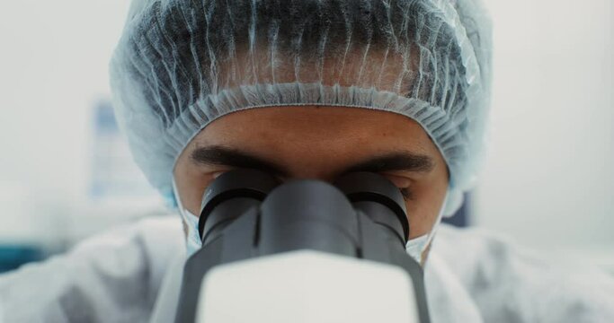 A scientist in sterile clothing looks through a microscope