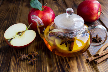 Tea with apple, cinnamon and anise in the glass teapot on the wooden background. Closeup.