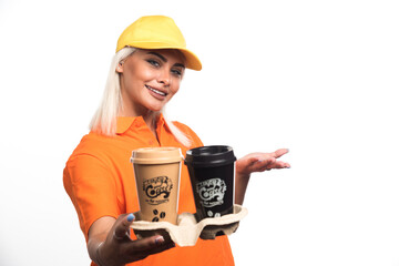 Female courier holding two cups of coffees on white background while smiling